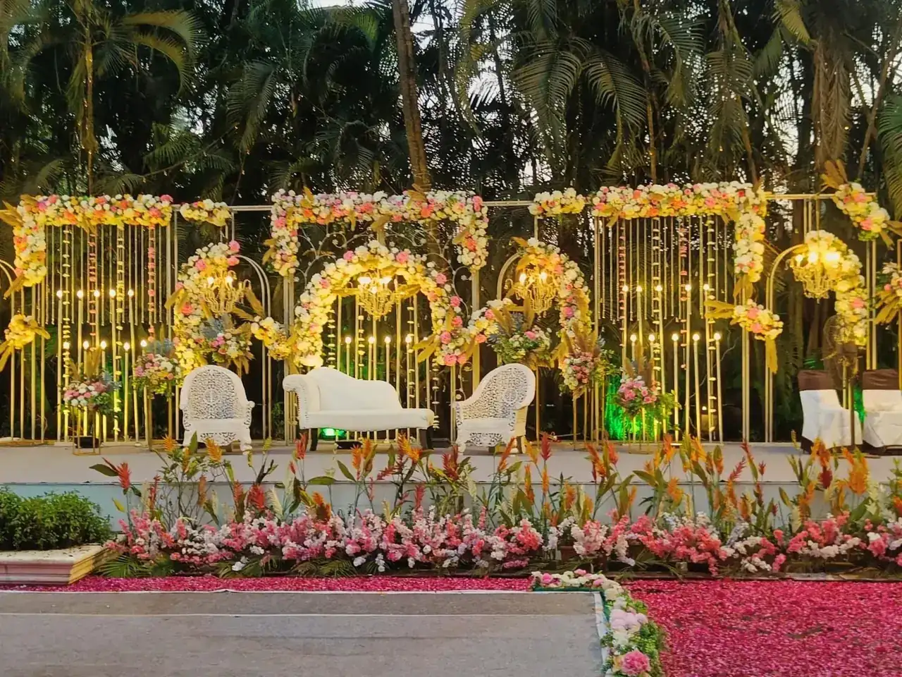 Grand reception stage with golden floral arches and white couches at Exotica