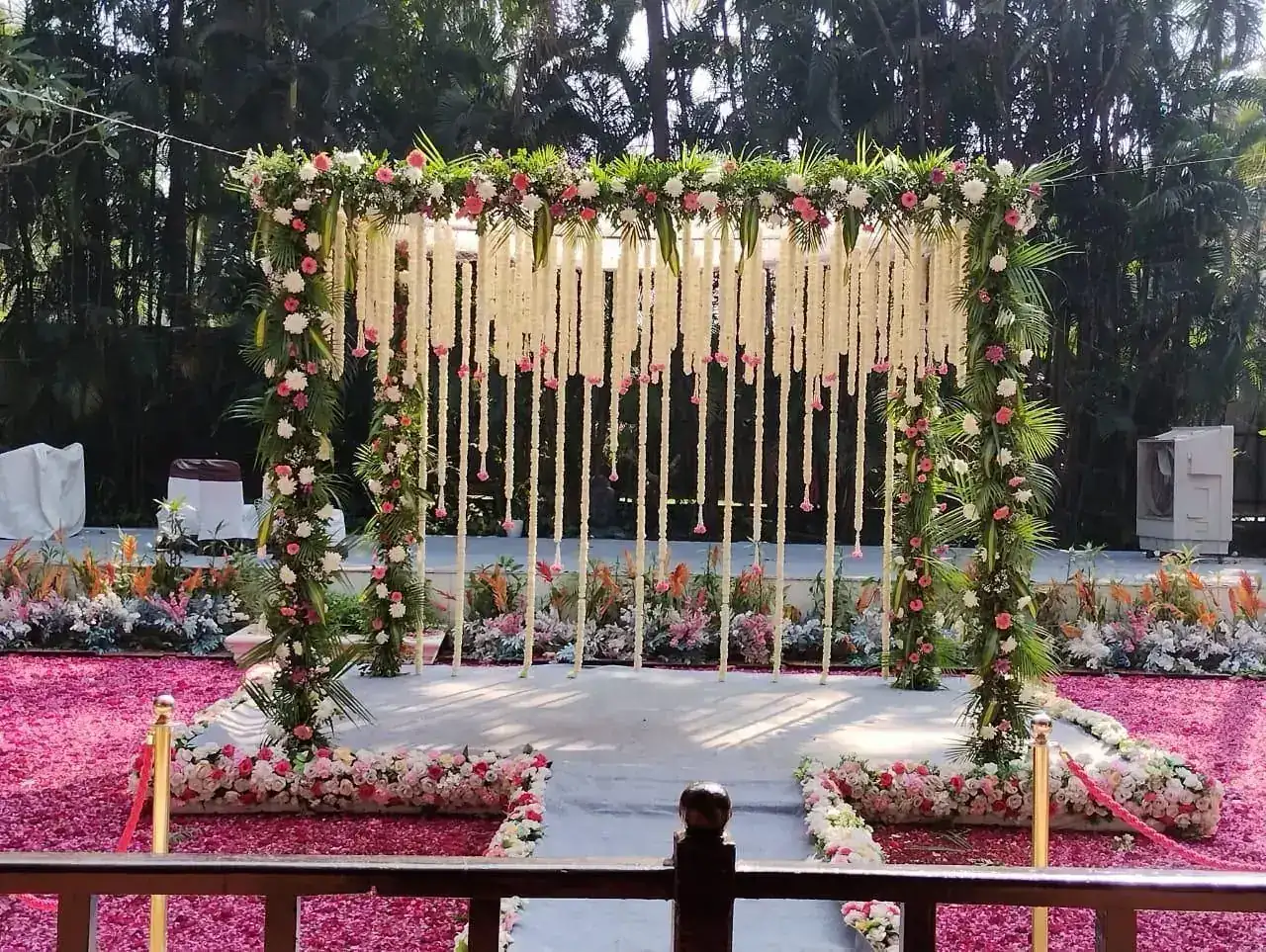 Wedding mandap with hanging white floral garlands over a petal-strewn stage at Exotica