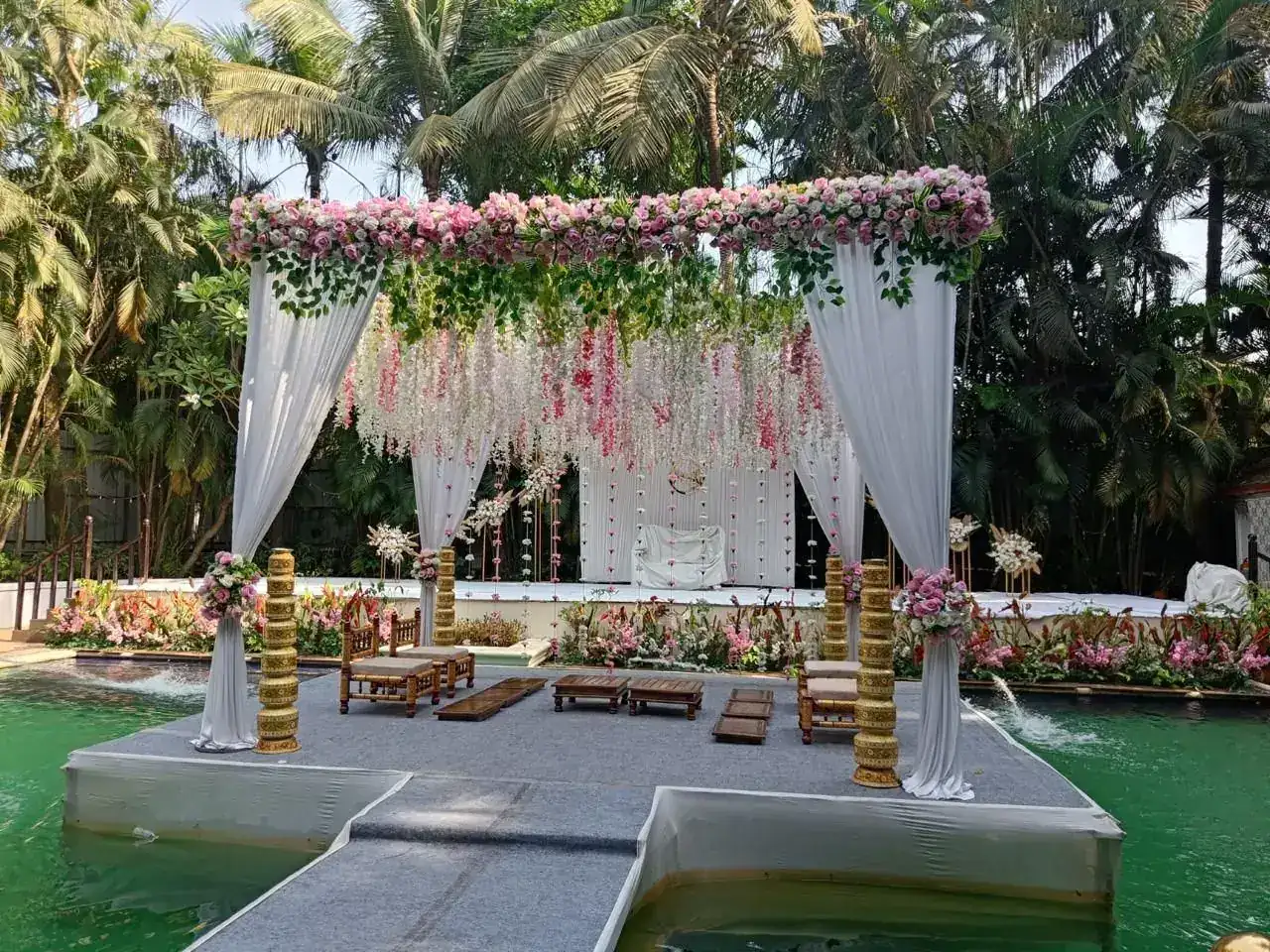 Pink and white floral mandap with drapes on the pool platform at Exotica