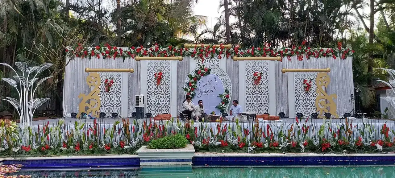 Poolside wedding stage with white backdrop and red floral arrangements at Exotica